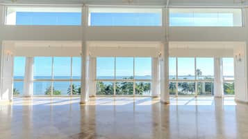 A spacious room with large windows offering a view of the ocean and palm trees.