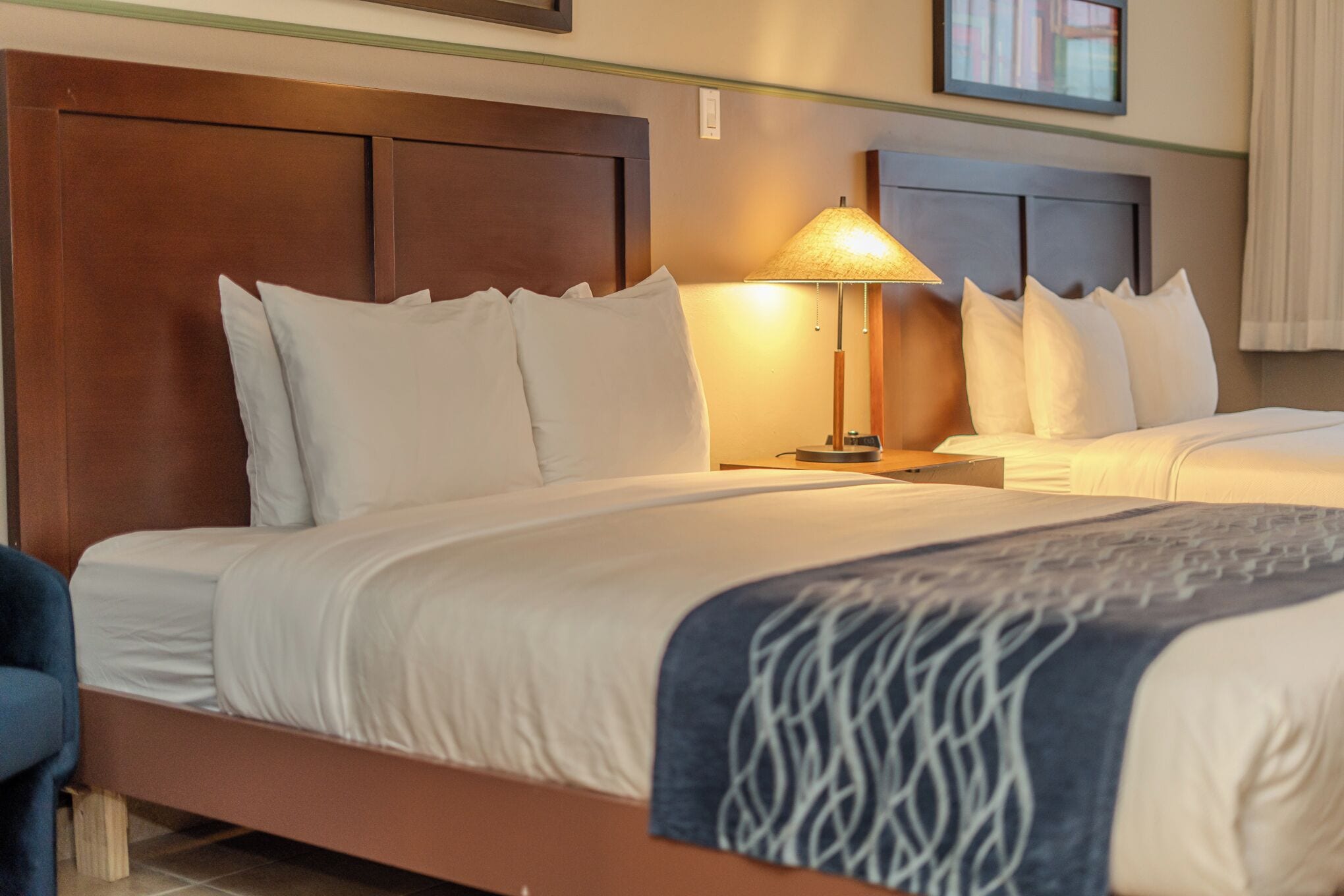 Une chambre d’hôtel avec deux lits, une tête de lit en bois, une lampe et une chaise bleue.