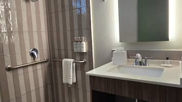 Un baño moderno con ducha, tocador y un espejo grande.