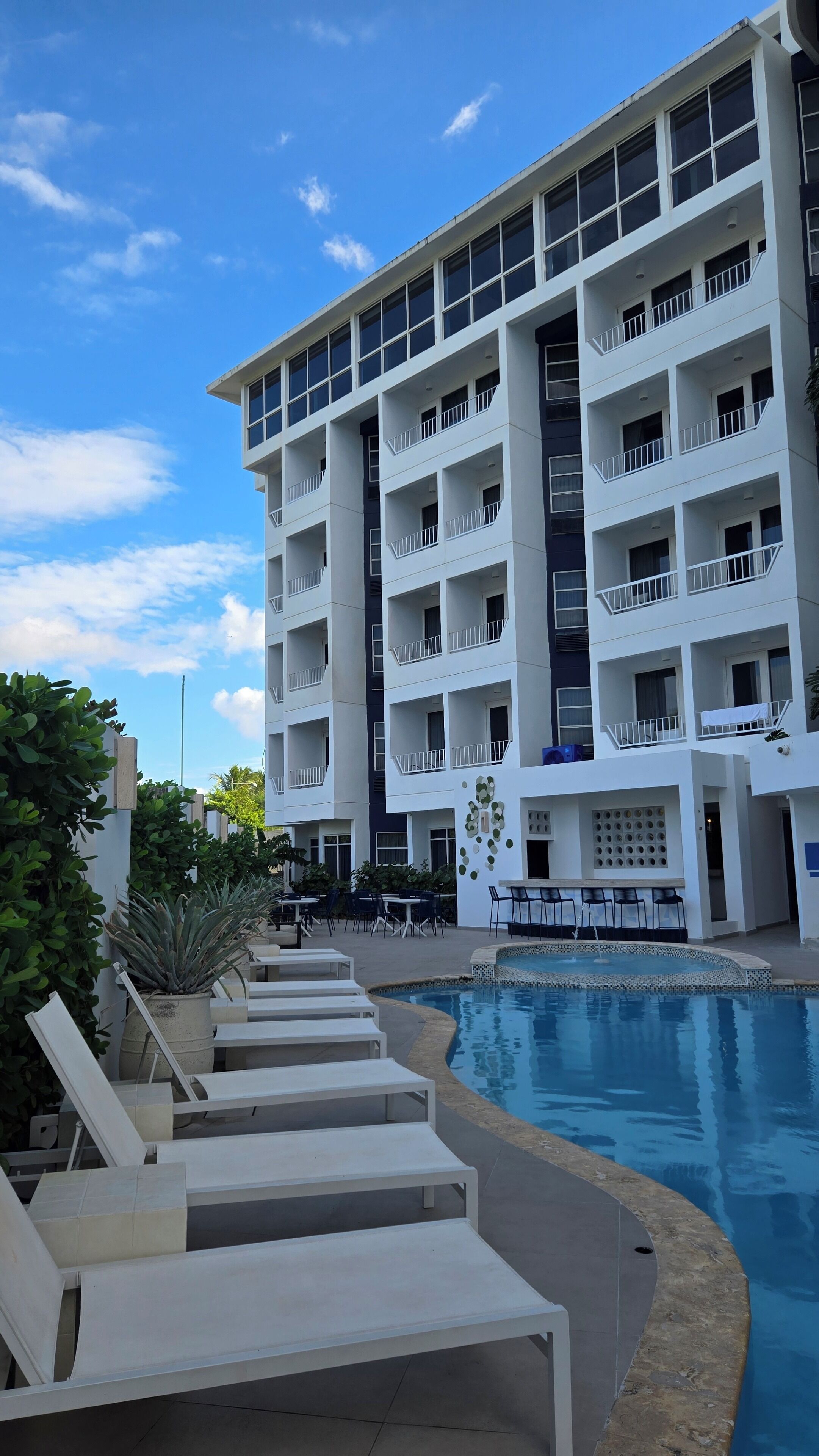 A modern hotel with multiple balconies, a swimming pool, and outdoor seating areas.