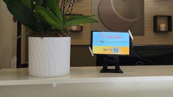Una reception con un vaso di orchidea e uno schermo digitale che mostra un messaggio promozionale.