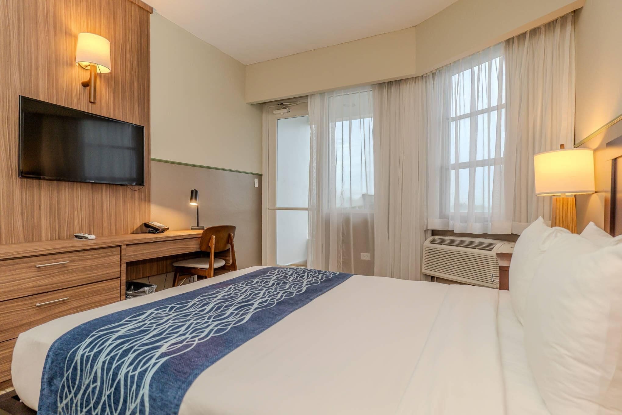 A hotel room with a bed, a desk, a chair, a TV, and a window with curtains.