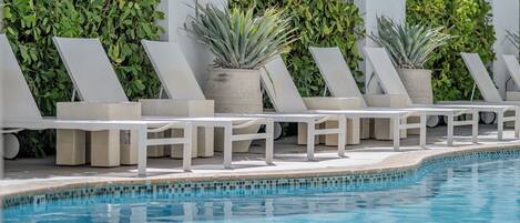 Zona de piscina con sillas reclinables blancas y macetas con follaje verde.