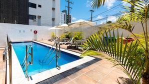 A swimming pool with a metal ladder, lounge chairs, umbrellas, and potted plants. - Praiamar Ponta Negra Hotel (Natal)