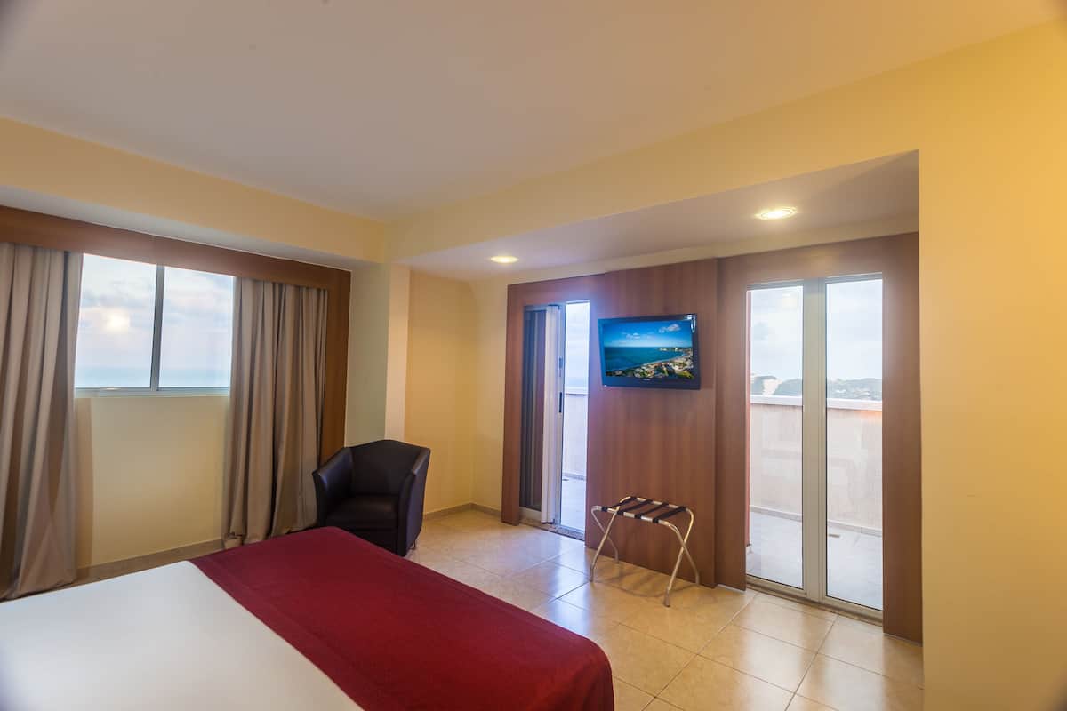 A hotel room with a bed, a chair, a TV, and a balcony with a view.