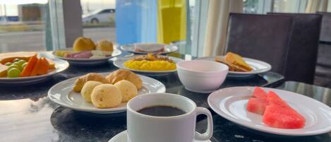 A breakfast table with various dishes, a cup of coffee, and a view of the street outside.