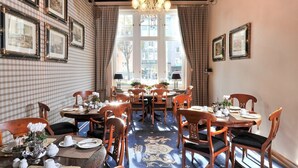 A dining area with wooden tables and chairs, a chandelier, and framed pictures on the walls. - Hotel Windsor (Düsseldorf)