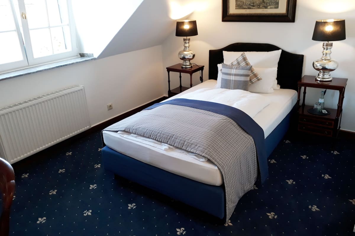 A bedroom with a bed, two bedside tables, a window, a radiator, and a framed picture on the wall.