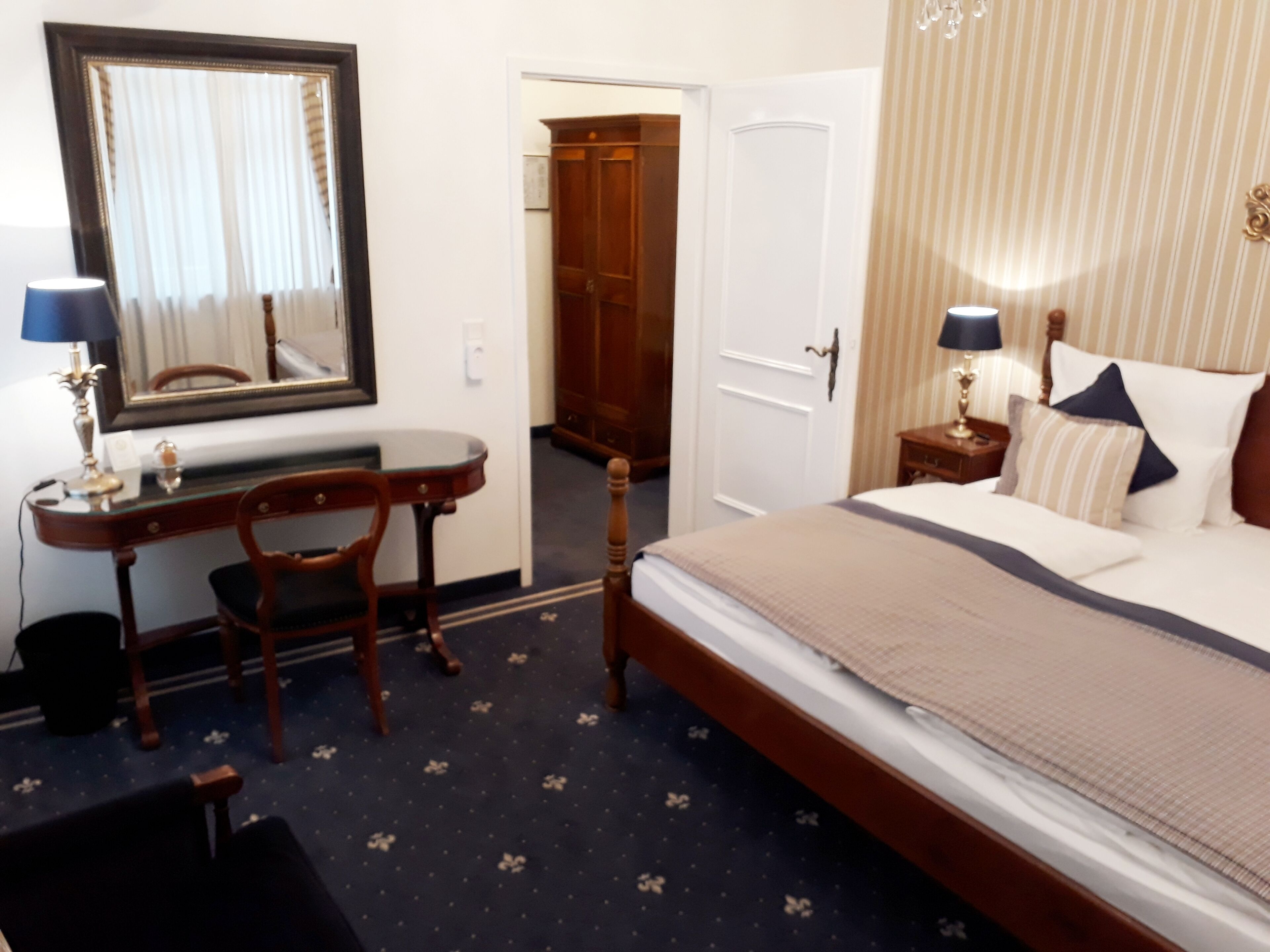 Una habitación de hotel con cama, escritorio, silla, espejo y armario.