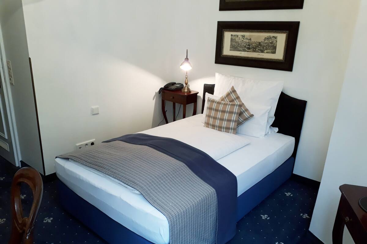 A neatly made bed with a blue and white bedspread, a patterned throw, and a bedside lamp.
