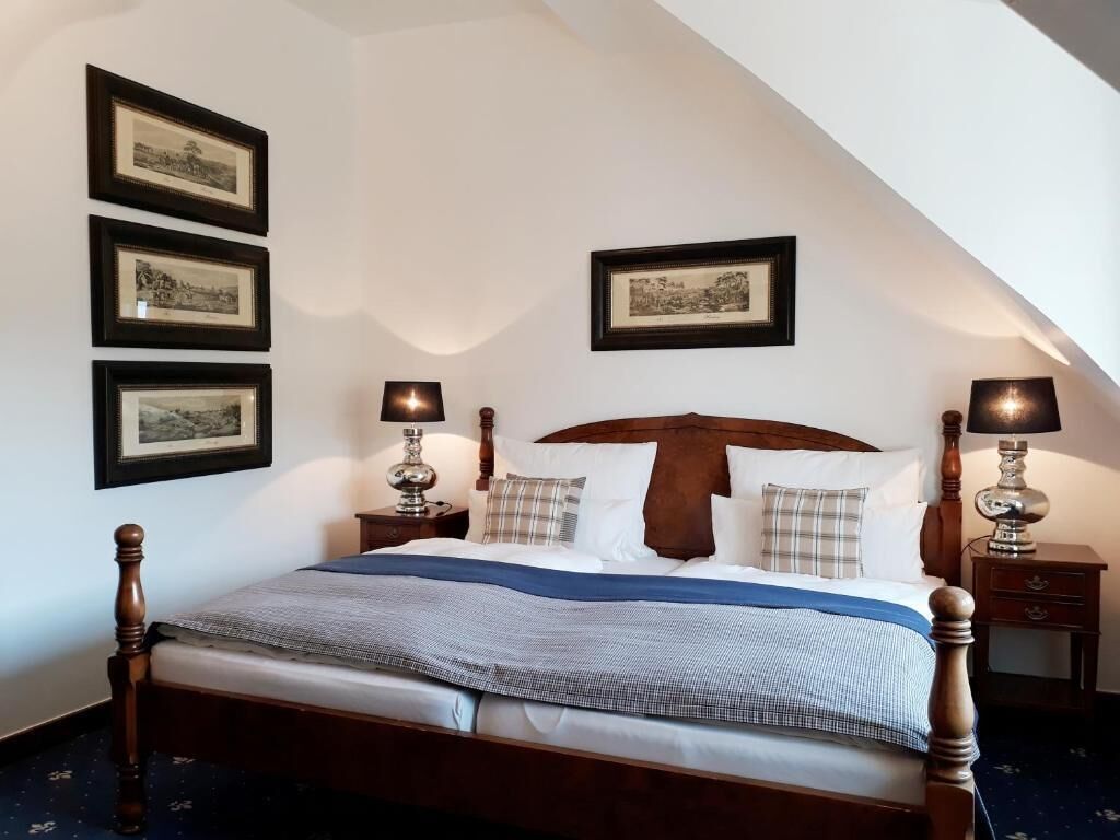 A bedroom with a wooden bed, two bedside tables with lamps, and three framed pictures on the wall.