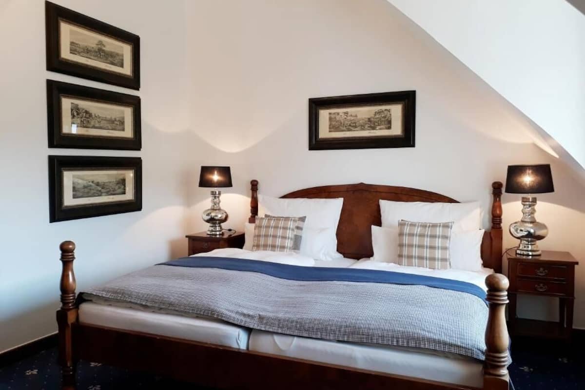 A bedroom with a wooden bed, two bedside tables with lamps, and three framed pictures on the wall.