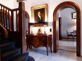 Una imponente escalera, una consola de madera con una lámpara y un retrato enmarcado encima.