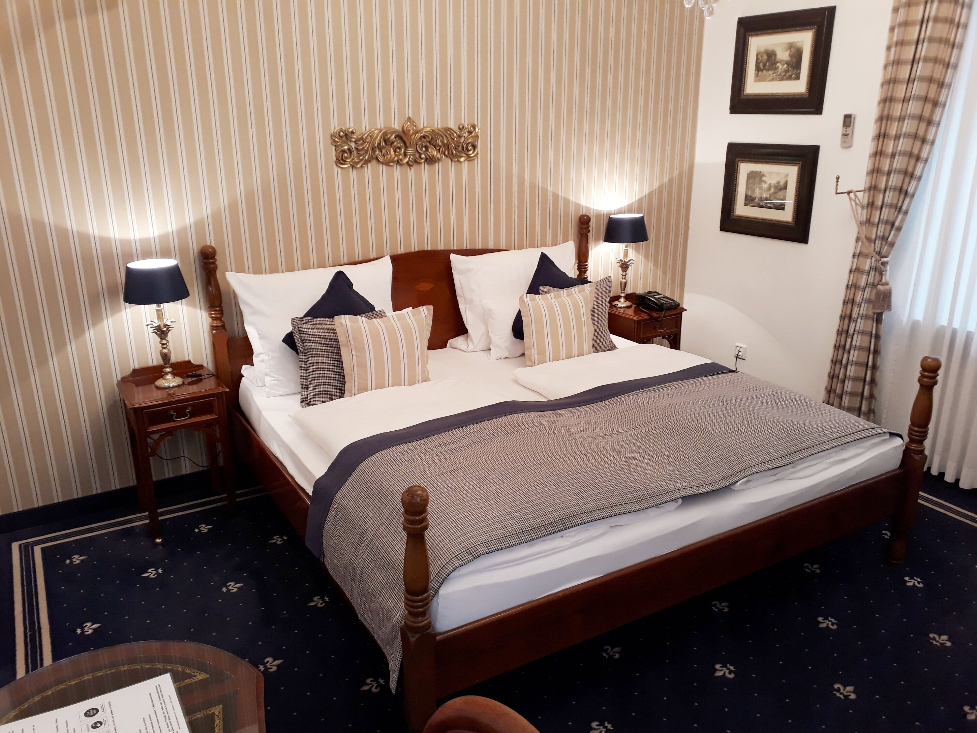 A neatly made bed with a dark headboard, a wooden nightstand with a lamp, and a wall with framed pictures.