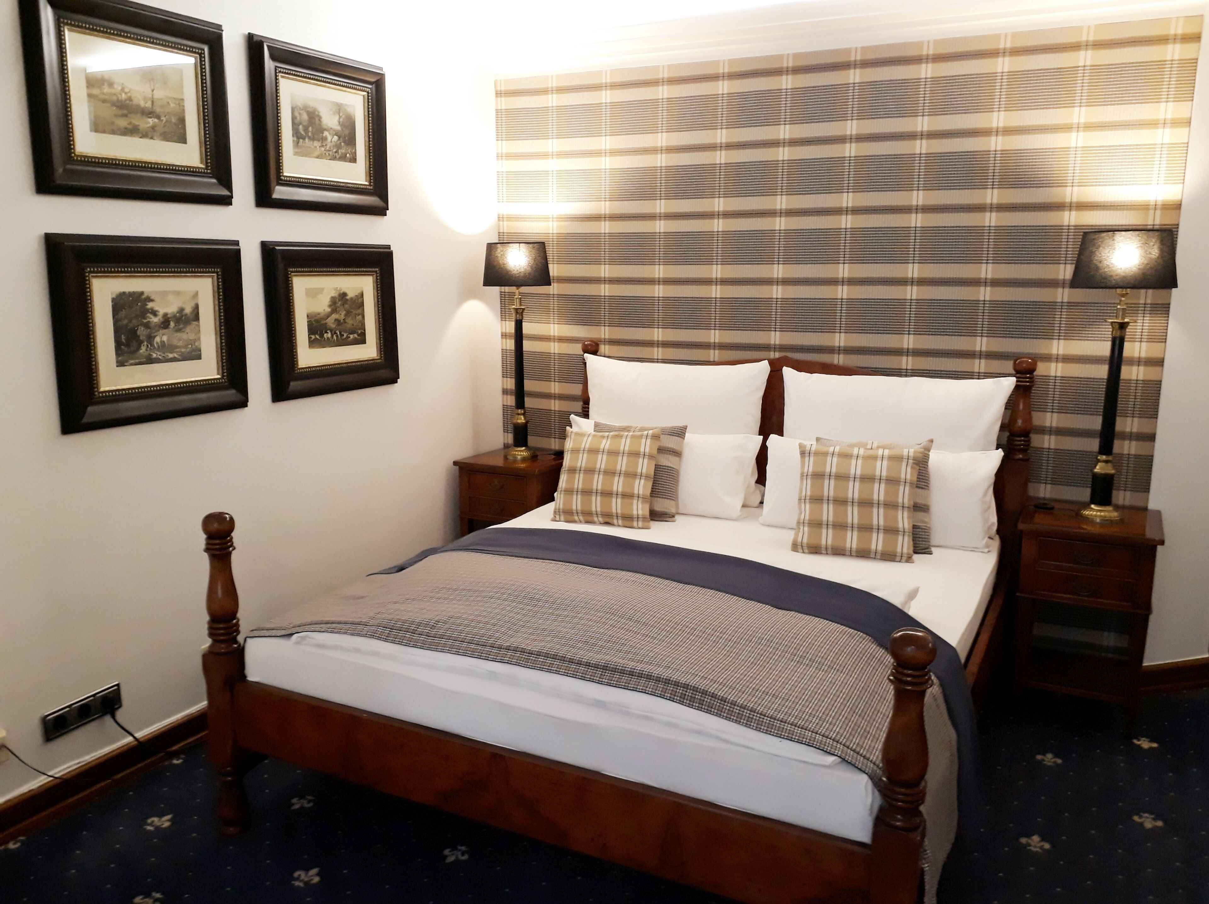 Cama bem arrumada com cabeceira xadrez, quadros nas paredes e abajures em cada lateral.