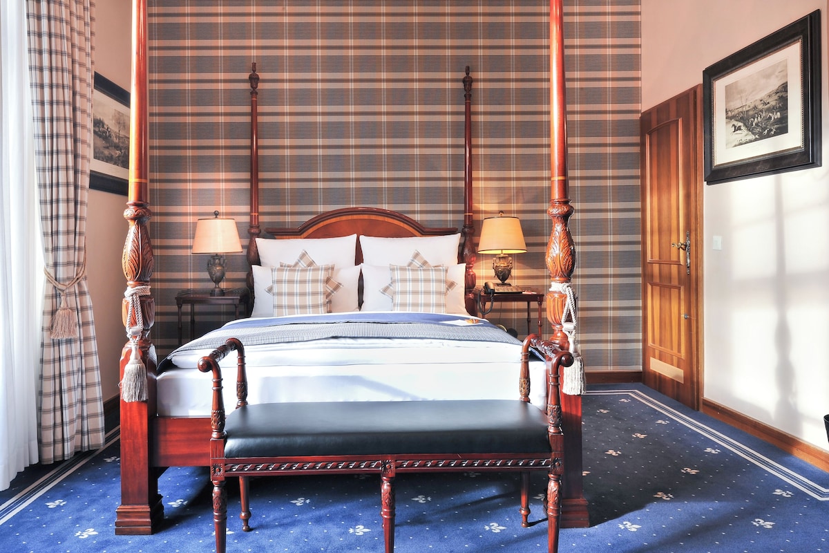 A four-poster bed with a wooden frame, two bedside lamps, and a plaid-patterned bedspread.