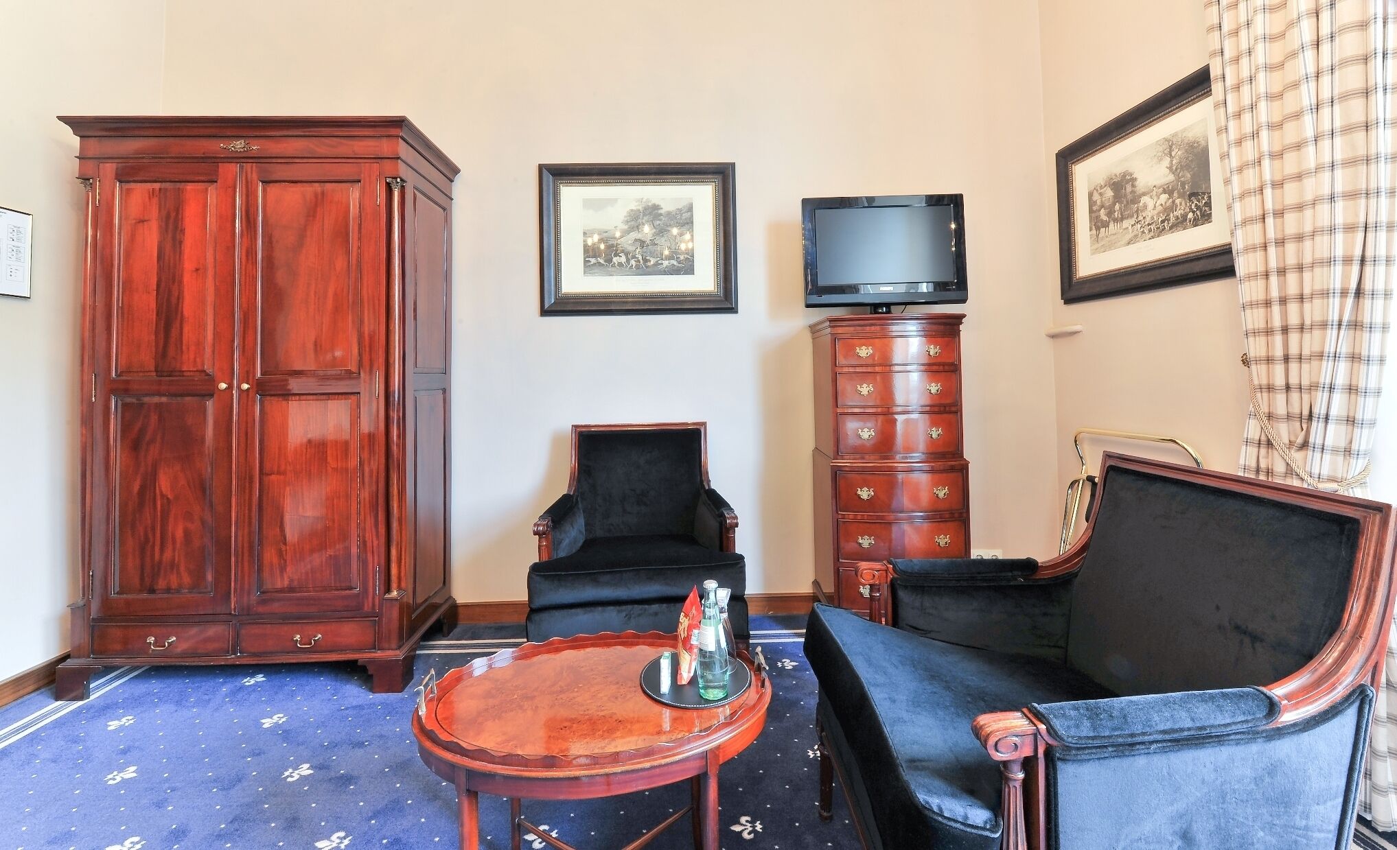 Une pièce comprenant une grande armoire en bois, un fauteuil noir, un canapé bleu, une petite table en bois et un téléviseur posé sur un meuble.
