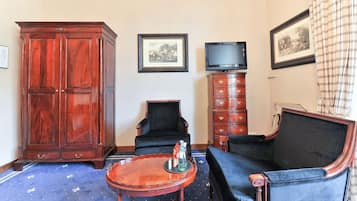 Une pièce comprenant une grande armoire en bois, un fauteuil noir, un canapé bleu, une petite table en bois et un téléviseur posé sur un meuble.