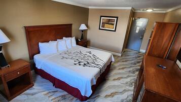 Habitación de hotel con una cama, dos mesitas de noche con lámparas, un aparador, un cuadro enmarcado en la pared y una puerta que da a otra habitación.