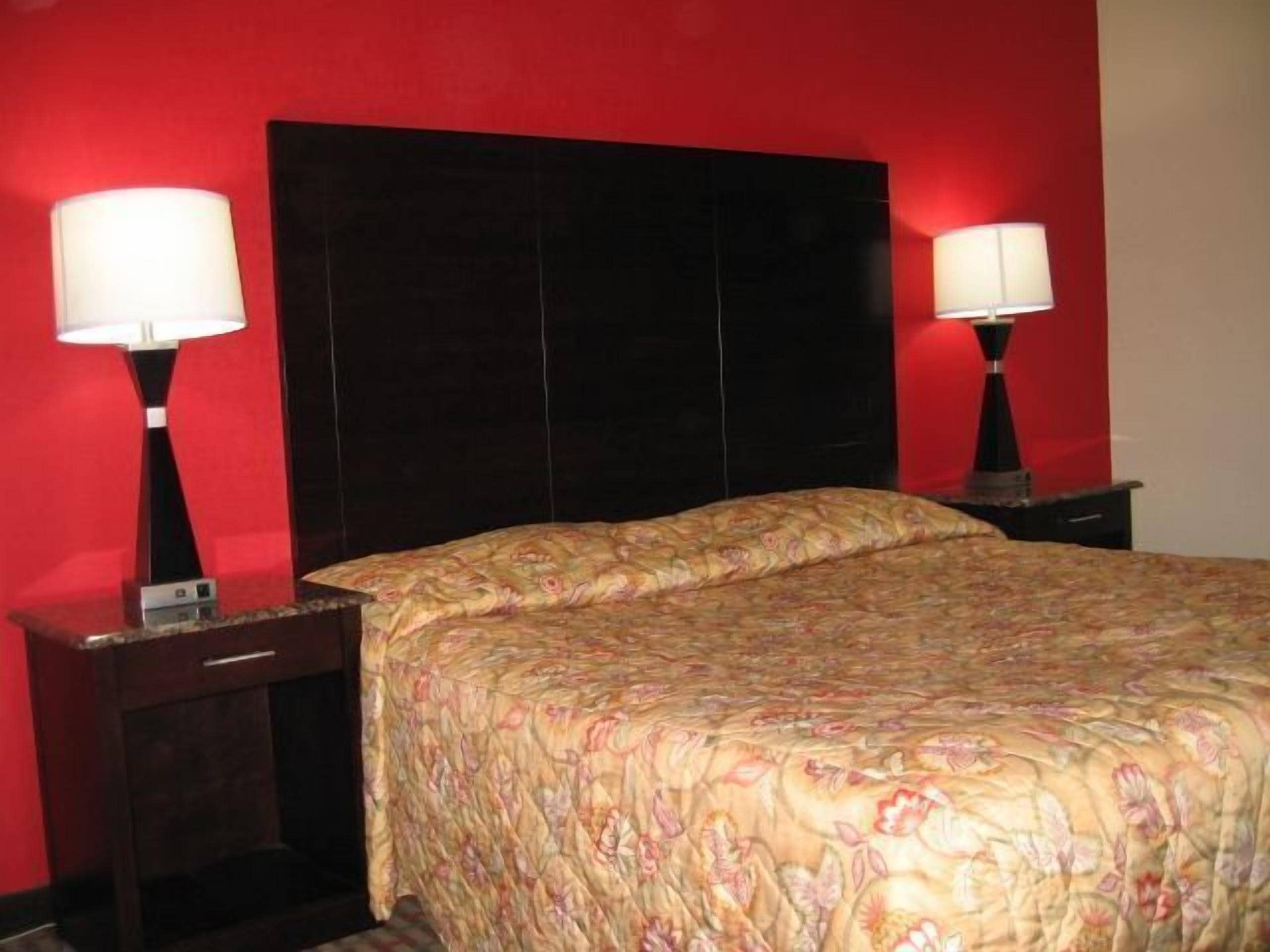 A hotel room with a large bed, two bedside tables, and a red wall.