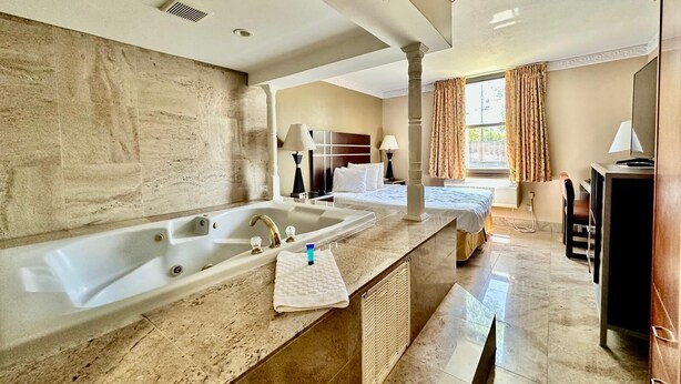 A hotel bathroom with a large bathtub, a sink, and a vanity area. - Townhouse Inn & Suites (Elmwood Park)