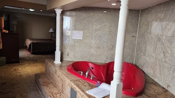 A bathroom with a red bathtub, marble flooring, and a large mirror.