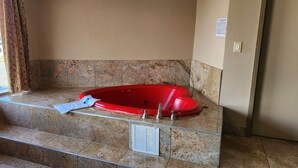 A red bathtub in a bathroom with a view of a street outside. - Townhouse Inn & Suites (Elmwood Park)