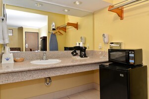 Un baño de hotel con lavamanos, espejo, toallero y un refrigerador negro.