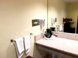 Un baño con lavamanos, espejo, secador de pelo y cafetera.