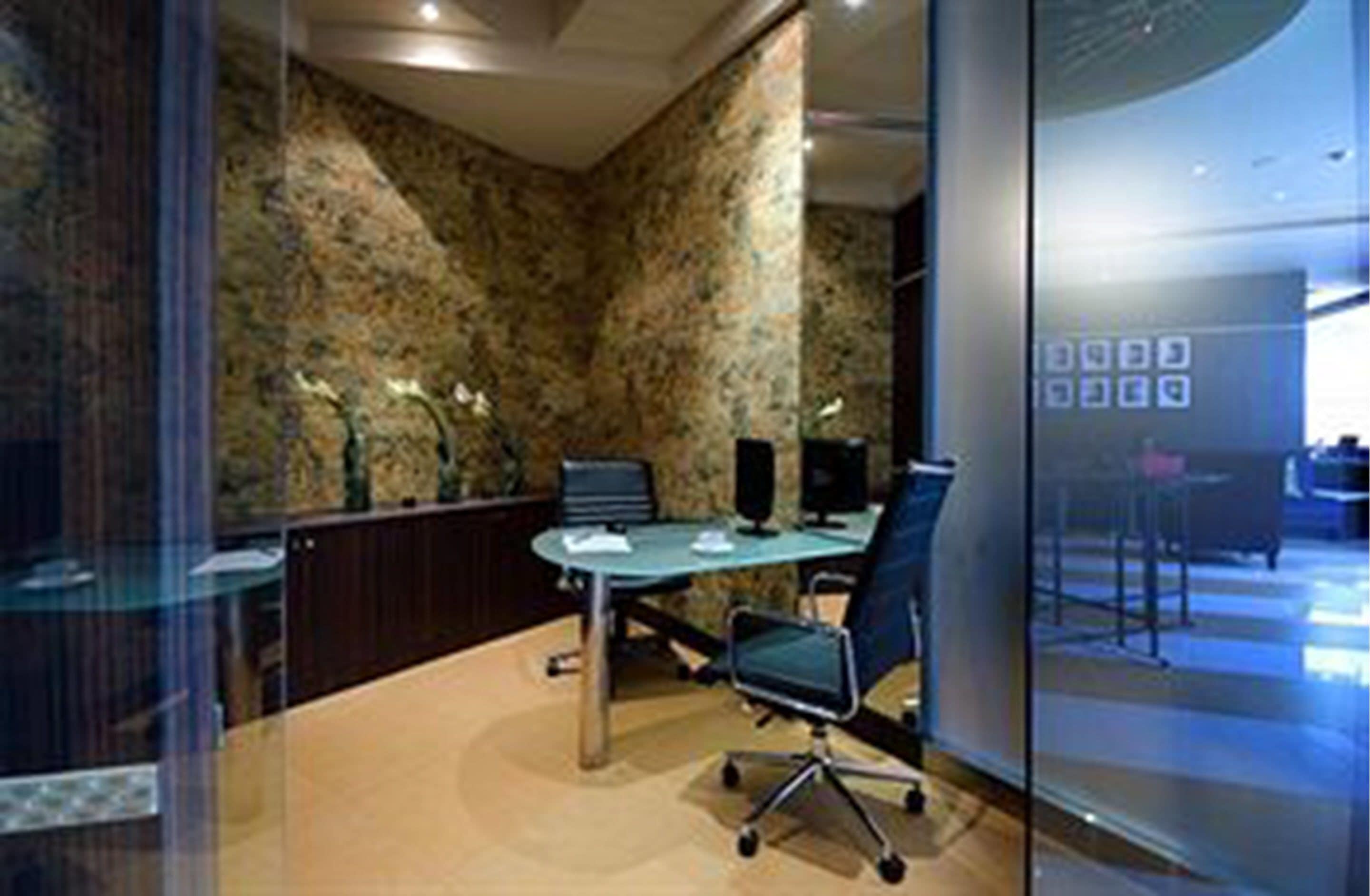 A conference room with a glass partition, a round table, and two chairs.