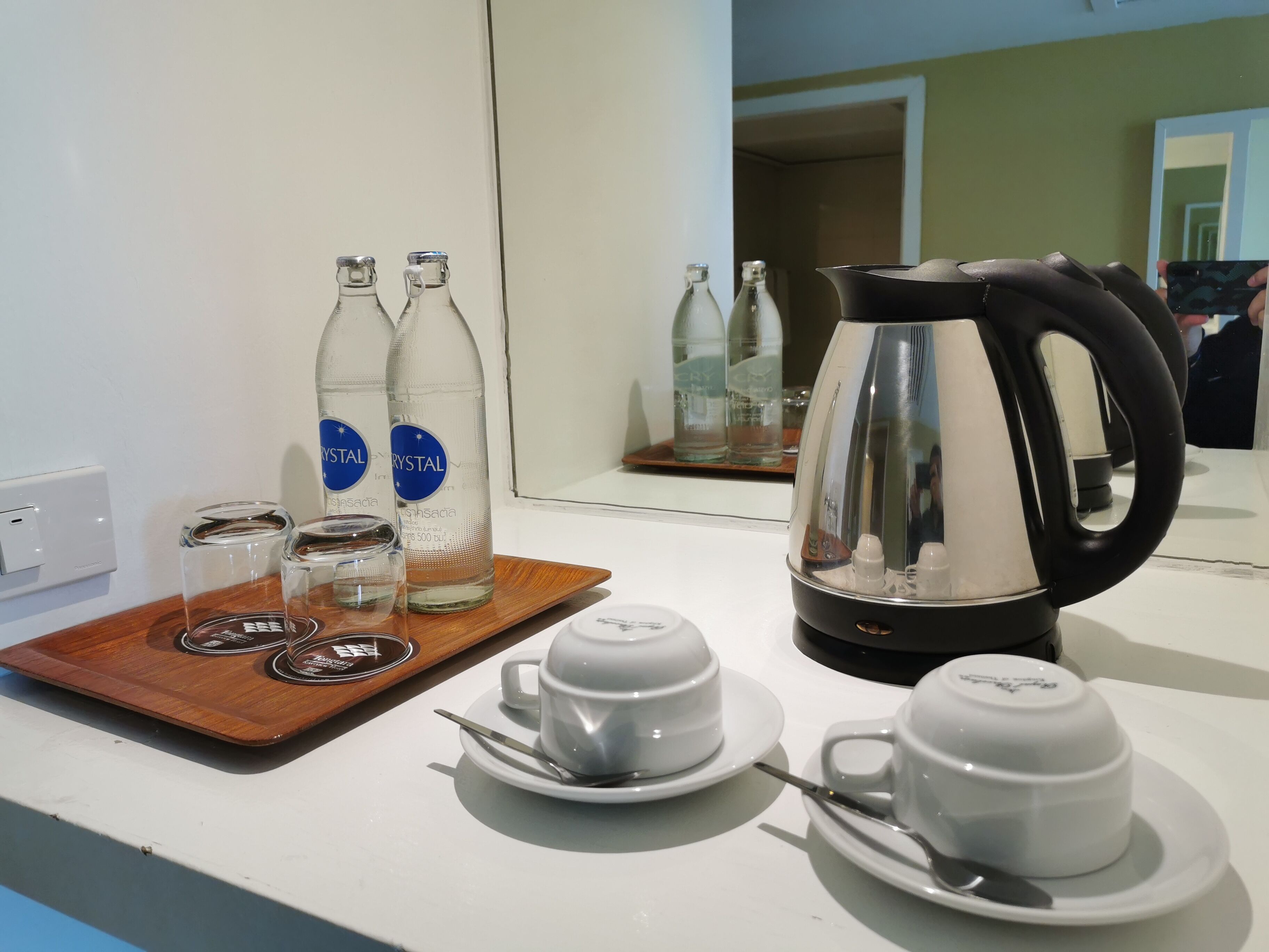 Dans une chambre d’hôtel, on trouve un plateau de petit-déjeuner avec une machine à café, deux bouteilles d’eau, ainsi qu’un plateau contenant des verres et une cuillère.