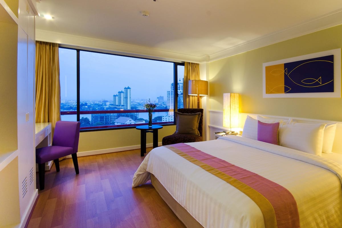 Une chambre d’hôtel avec un grand lit, un bureau, une chaise, une fenêtre donnant sur la ville et un tableau au mur.