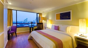 Una habitación de hotel con una cama grande, un escritorio, una silla, un ventanal con vistas a la ciudad y un cuadro en la pared.
