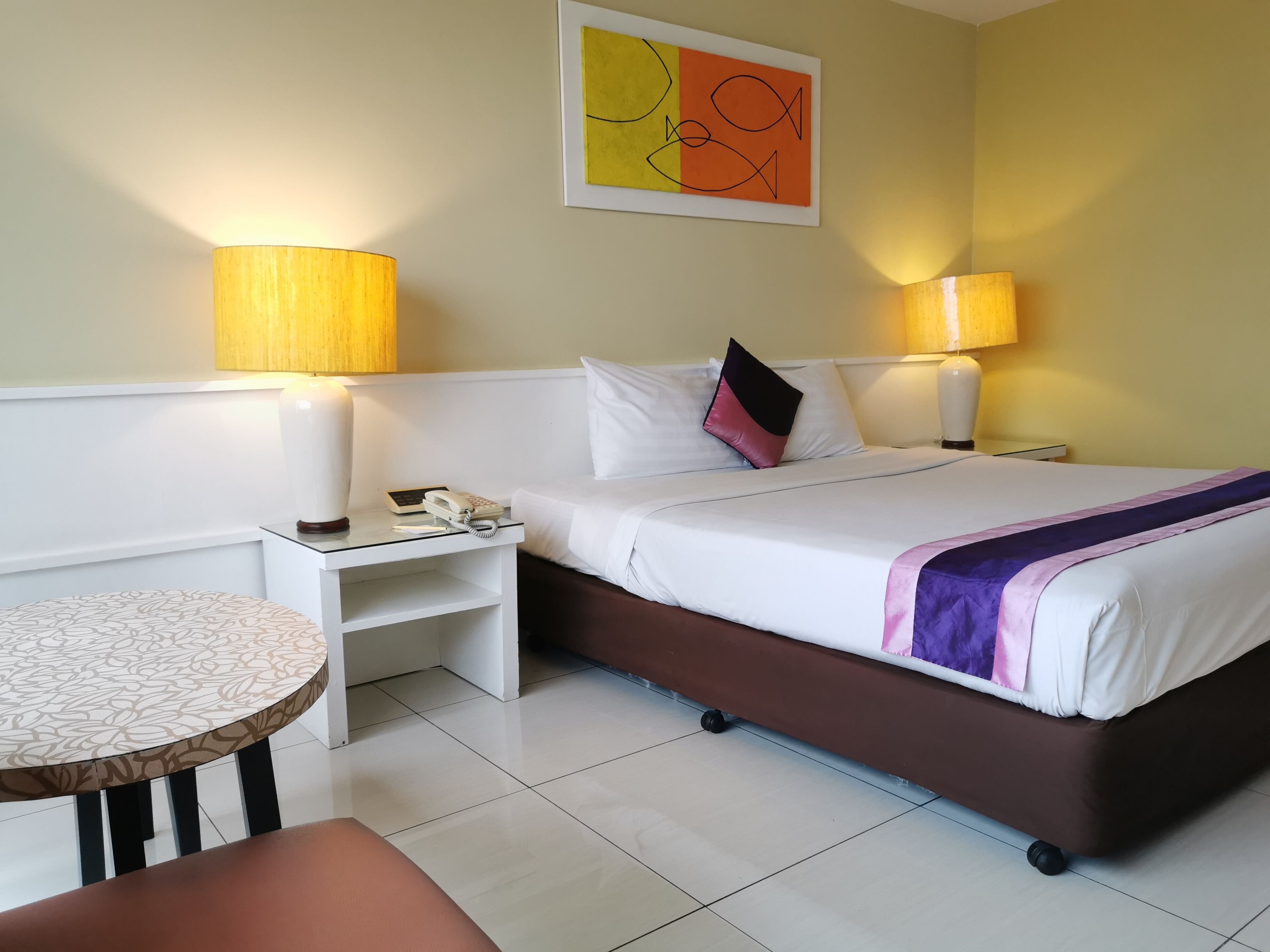 A hotel room with a bed, bedside lamps, a telephone, a small table, and a chair.