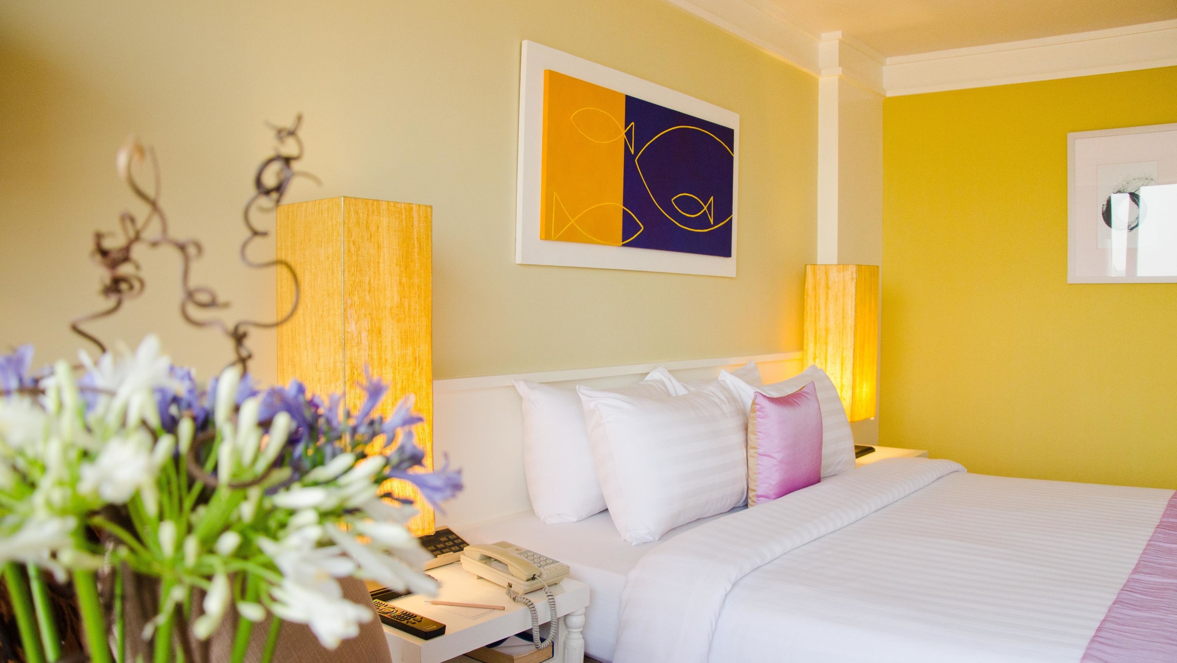 Una habitación de hotel con cama, mesita de noche, lámpara y una obra de arte enmarcada en la pared.
