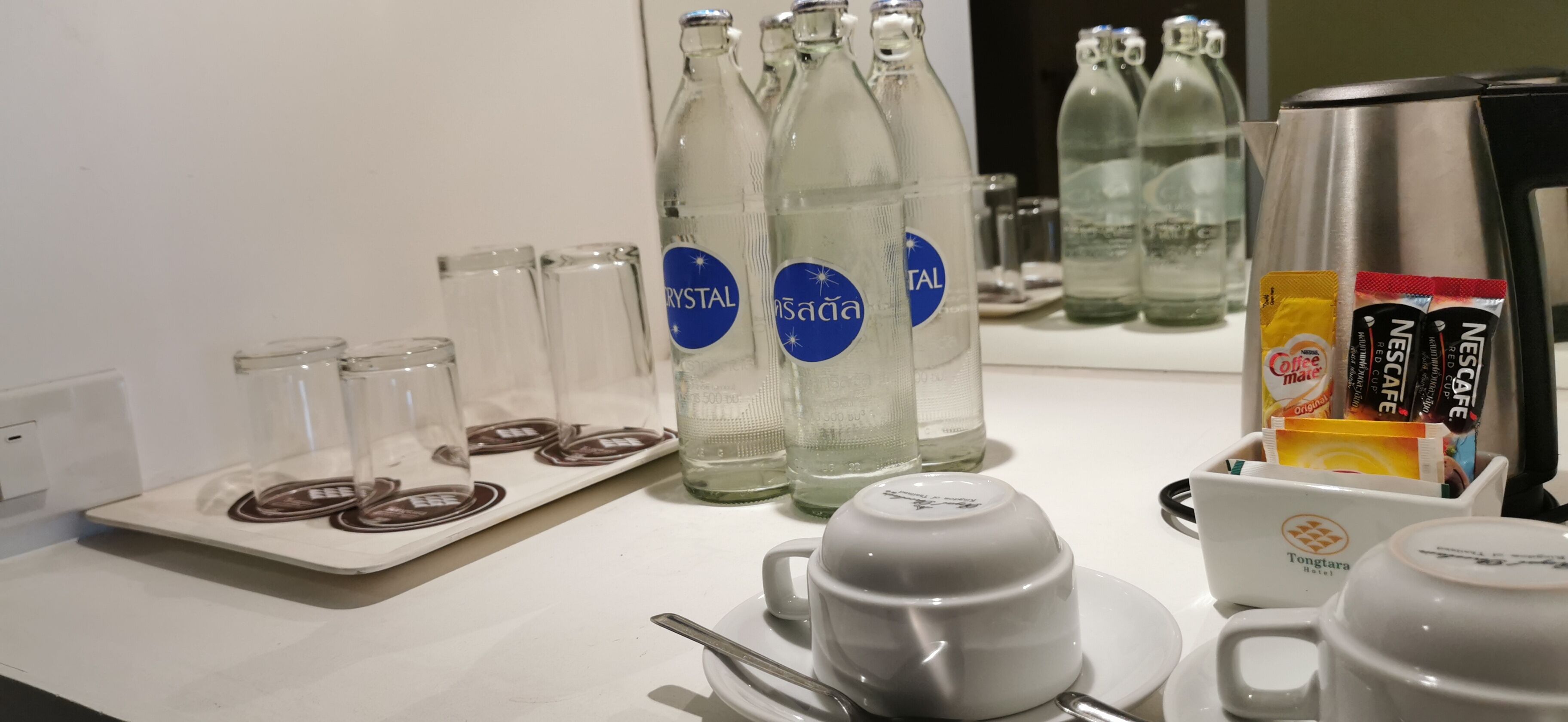 A table set with clear glasses, a white mug, and a coffee maker.