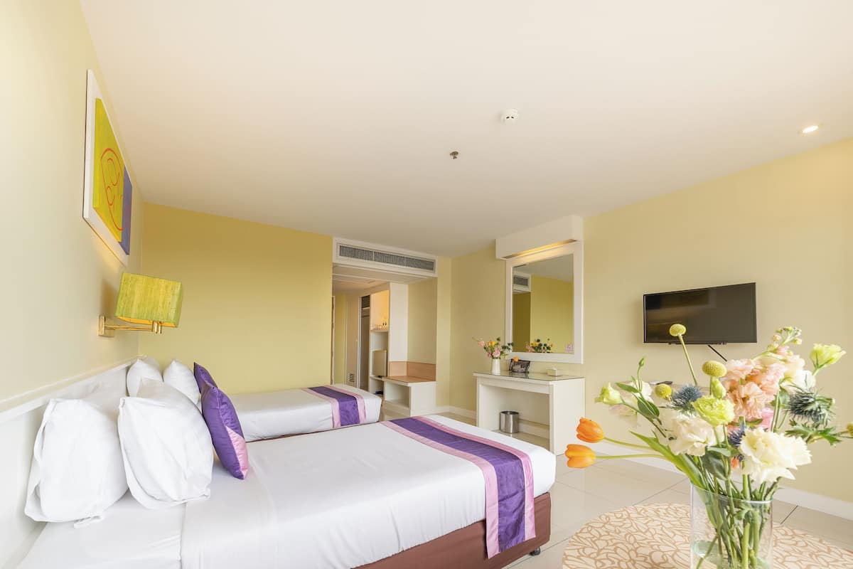 Une chambre d’hôtel avec un lit, un bureau, une télévision et un vase de fleurs.