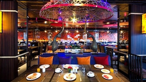 A restaurant with a modern interior, featuring a unique ceiling structure, vibrant wall art, and a variety of seating options including booths and tables.