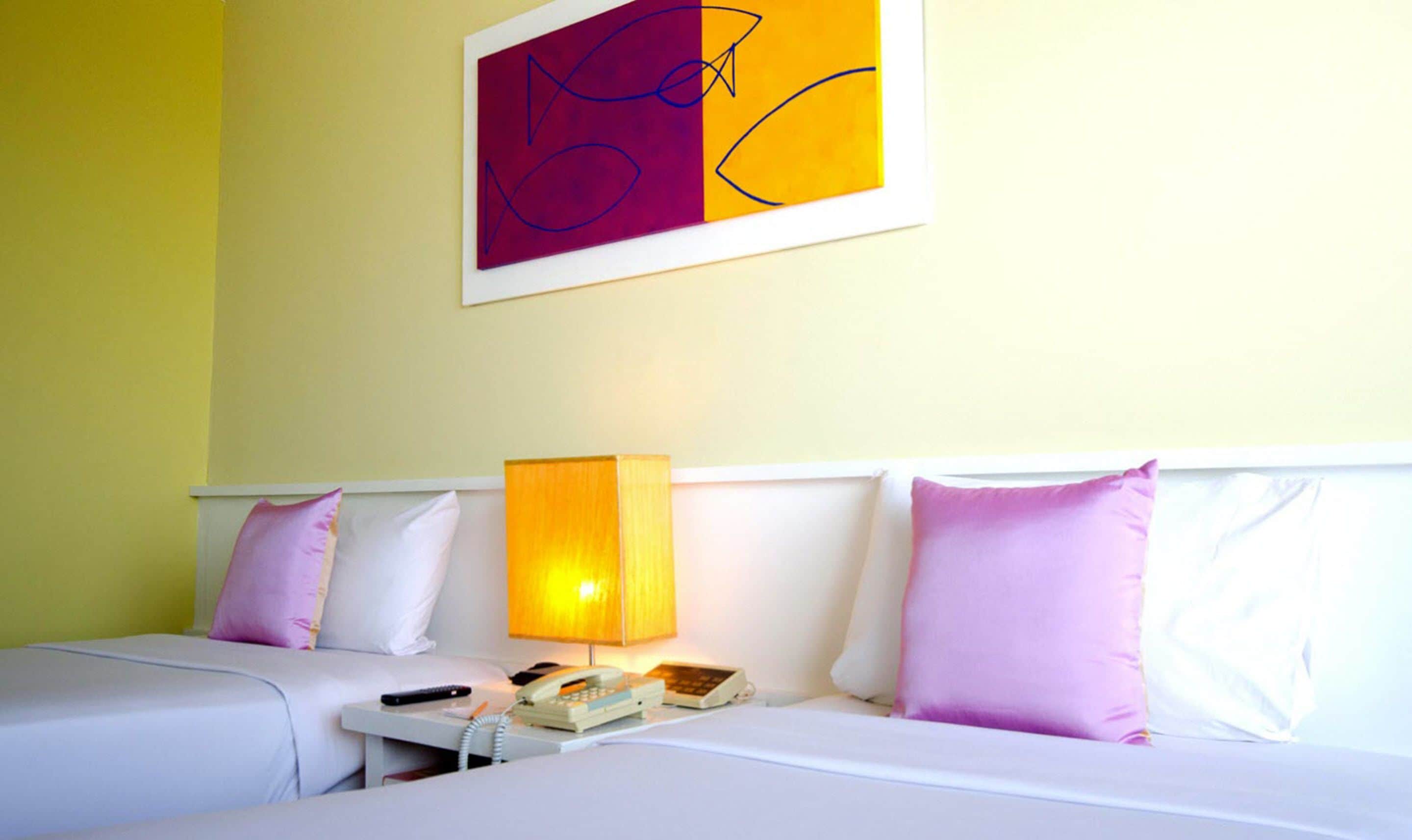 A hotel room with two beds, each with a white headboard, a bedside table with a lamp, and a phone.