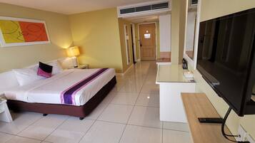 A hotel room with a bed, bedside table, lamp, TV, and a hallway leading to a door.