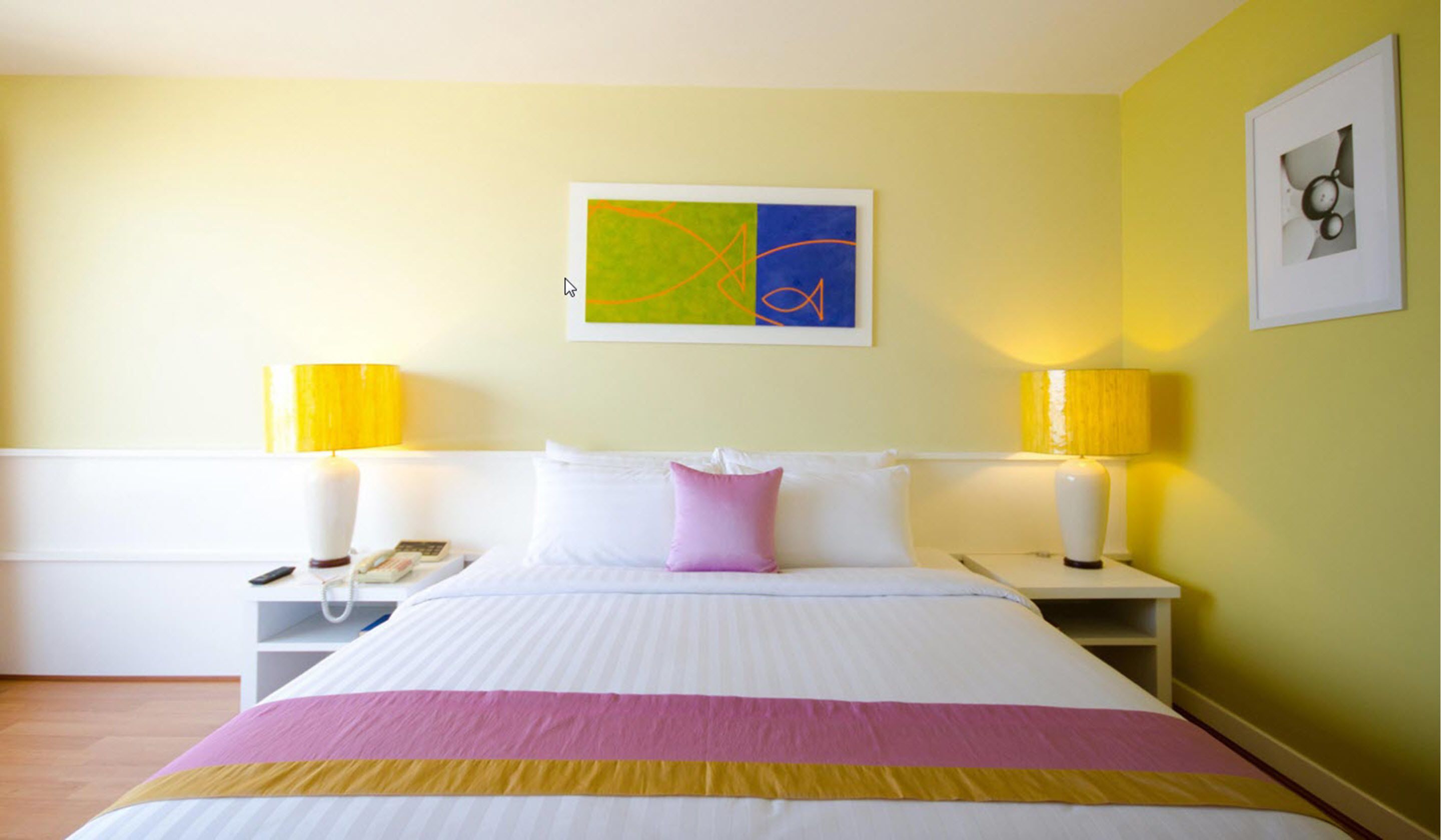 Habitación de hotel con una cama grande, dos lámparas de noche, una mesita de noche, un teléfono y un cuadro en la pared.