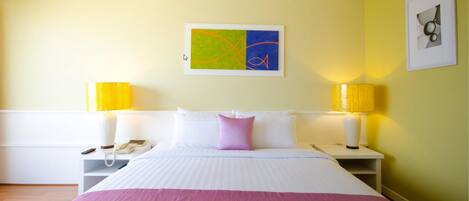 Habitación de hotel con una cama grande, dos lámparas de noche, una mesita de noche, un teléfono y un cuadro en la pared.