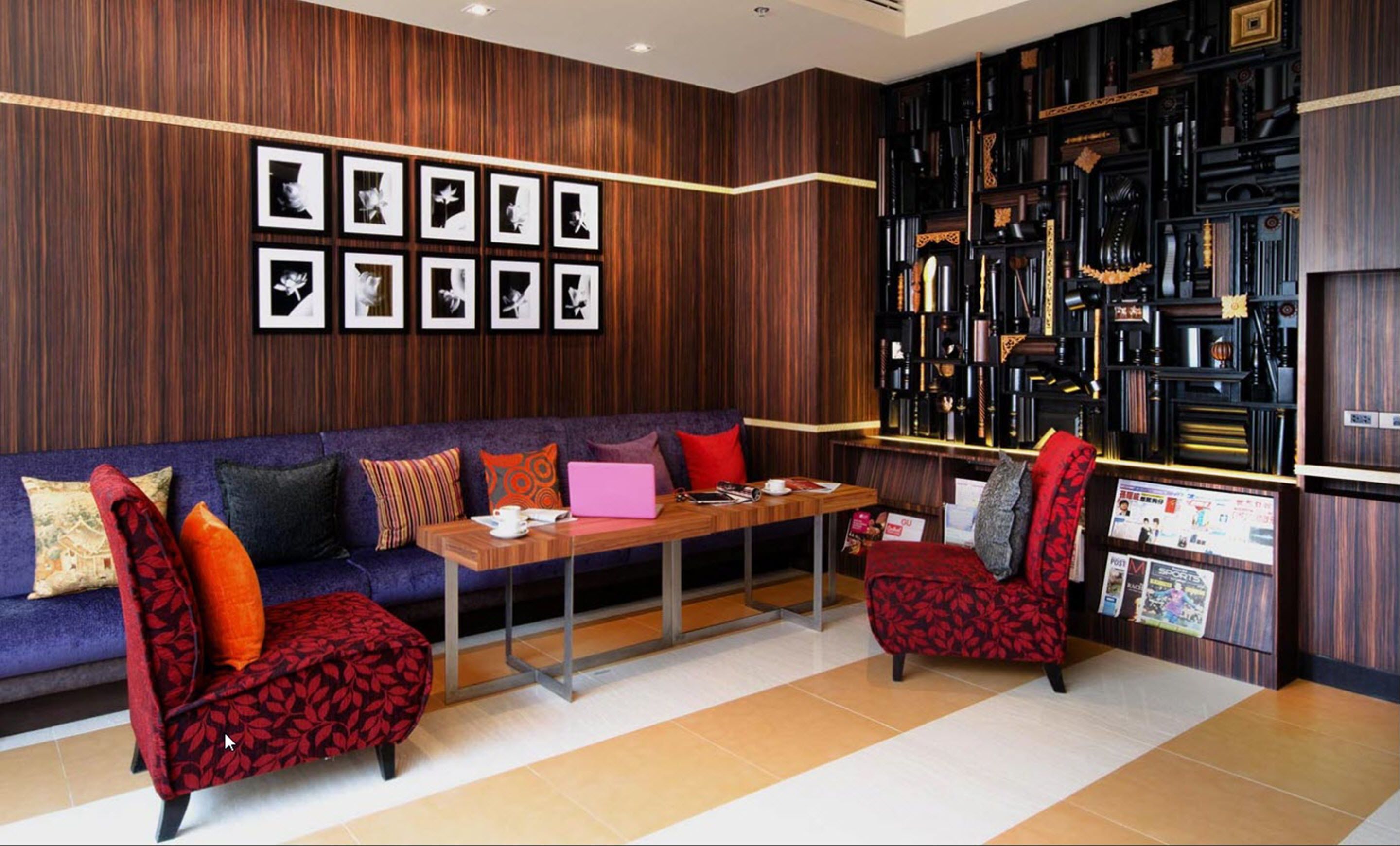 Een moderne zithoek met een houten wand, een bank, twee fauteuils, een salontafel en een boekenkast met diverse spullen.