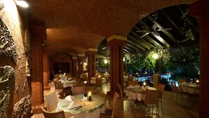 Un espacio de comedor al aire libre con paredes de ladrillo, mesas y sillas, que incluye un arco de ladrillo y un ventilador de techo.
