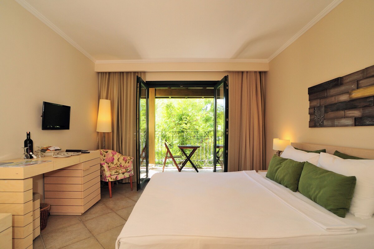 A hotel room with a bed, desk, chair, TV, and a balcony with a table and chair.