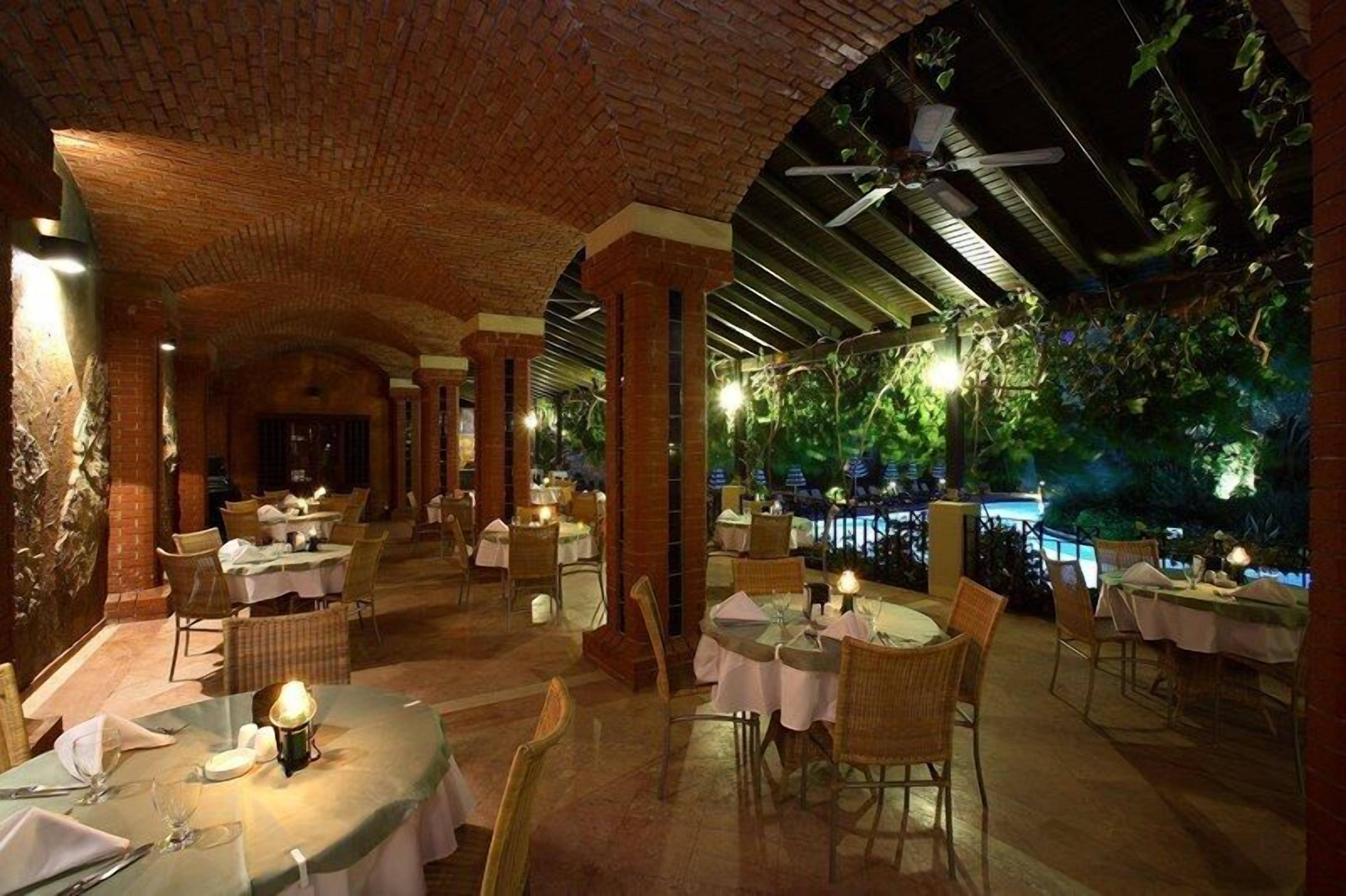 Un restaurante interior con arcos de ladrillo, mesas redondas y sillas.