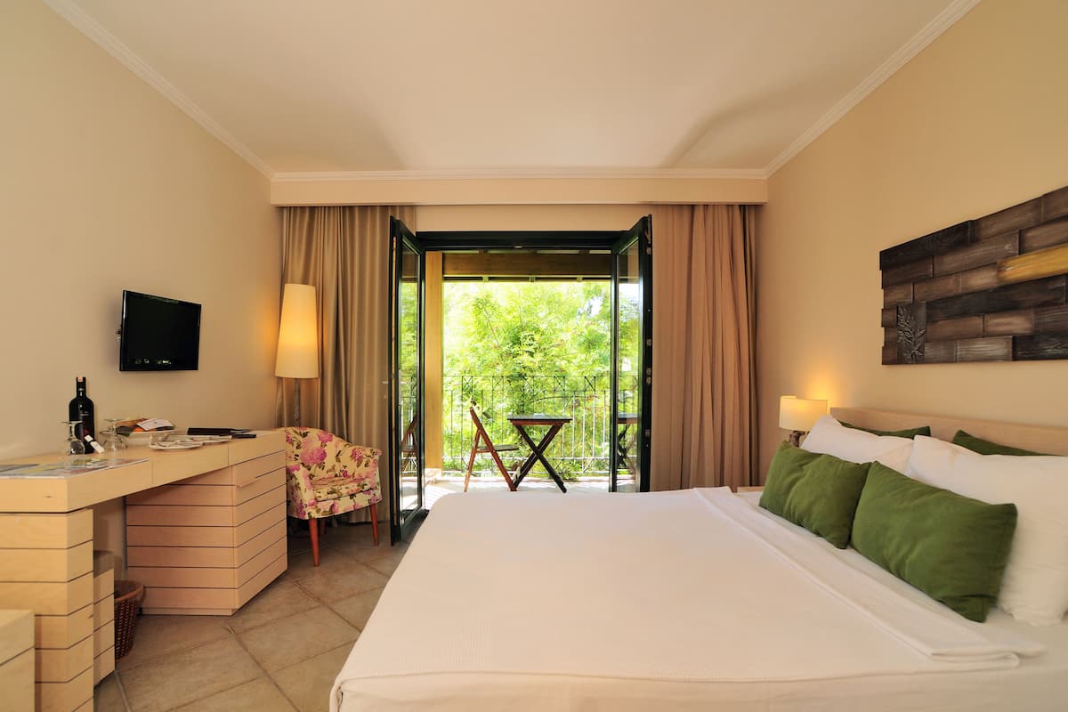 Habitación de hotel con cama, escritorio, silla, televisión y balcón con mesa y sillón.