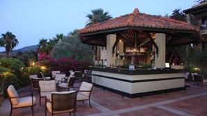 Un área de bar al aire libre con techo de tejas, rodeada de sillas y una barra.