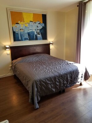 A bedroom with a large bed, a painting above the bed, and a nightstand with a lamp. - Hotel Tingis (Paris)