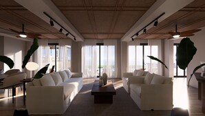 Un salón amplio con dos sofás blancos, una mesa de centro y ventanas grandes con cortinas translúcidas.